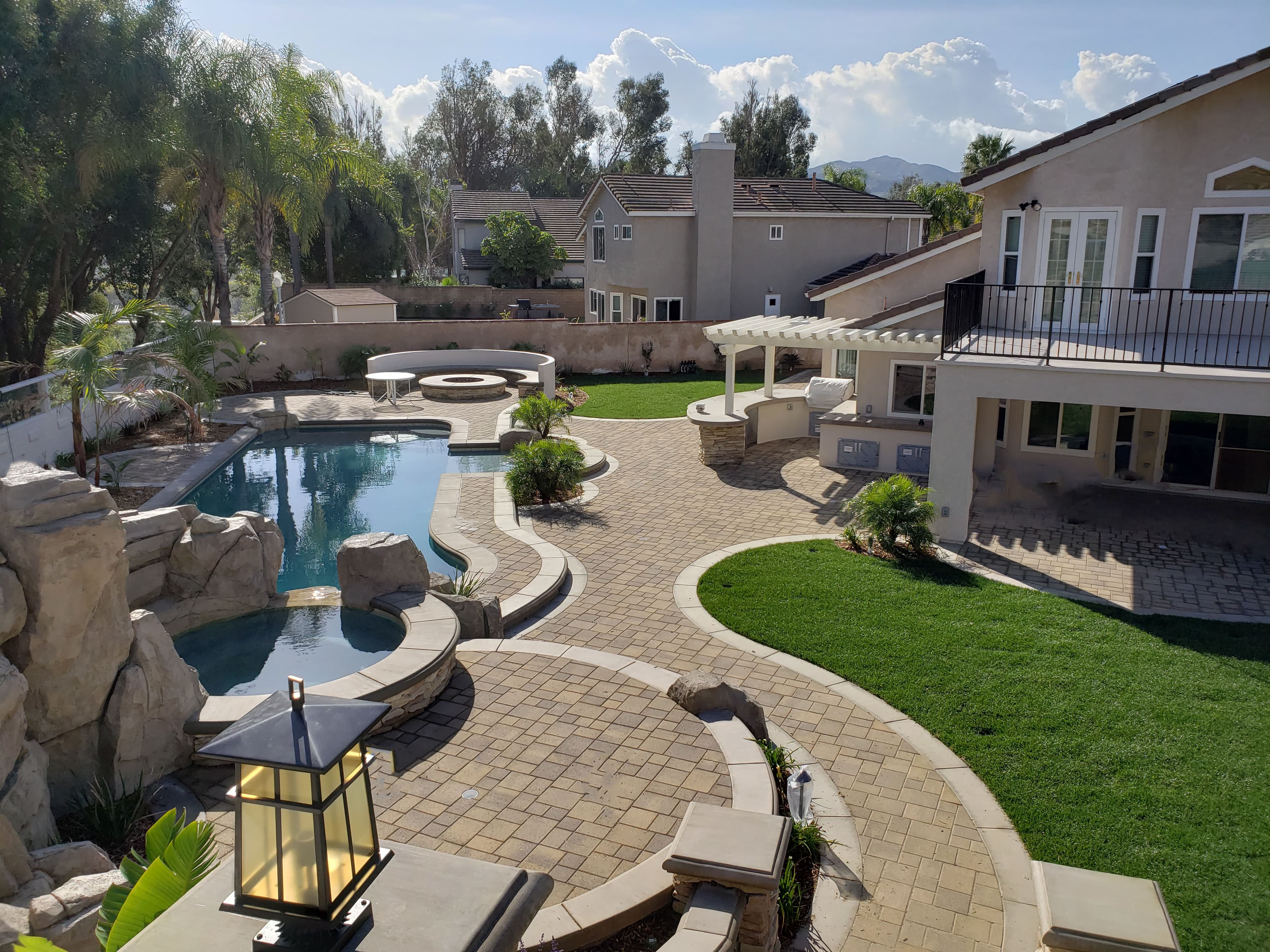 Luxurious backyard featuring a curved swimming pool, stone patio, outdoor kitchen, and lush green lawn.