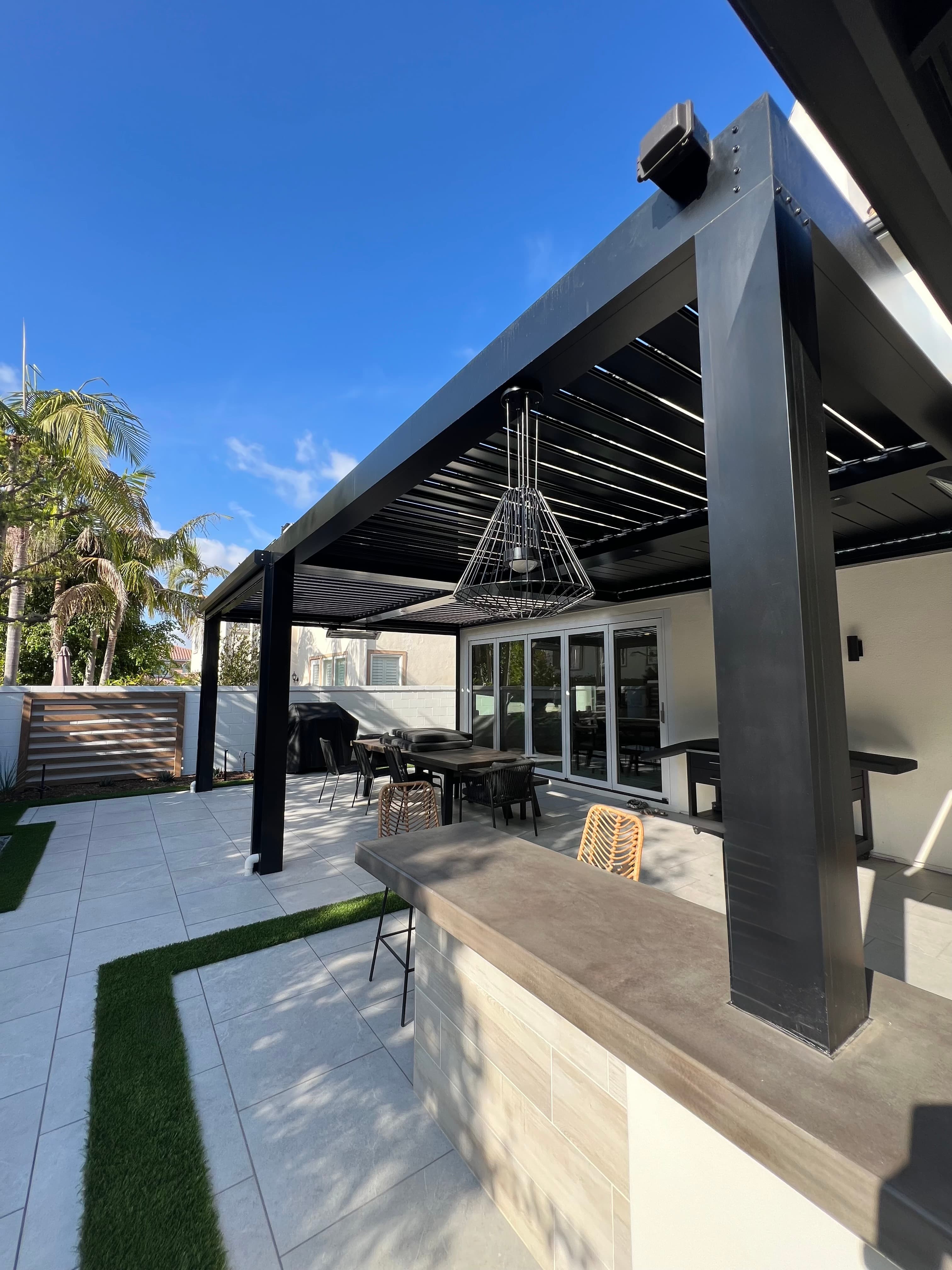 Modern black louvered pergola shading a patio with a concrete bar and outdoor dining area.